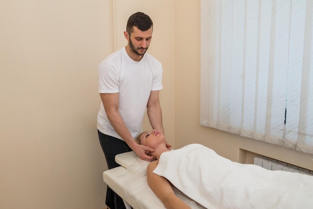 Beautician or masseur doing manual relaxing anti-aging massage of the neck and shoulders for a young woman in a beauty salon.