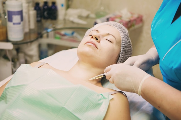 Beautician performs a needle mesotherapy treatment on a woman's face And neck area