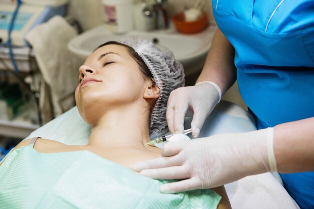 エステティシャンが女性の顔と首の部分に針メソセラピー治療を行います