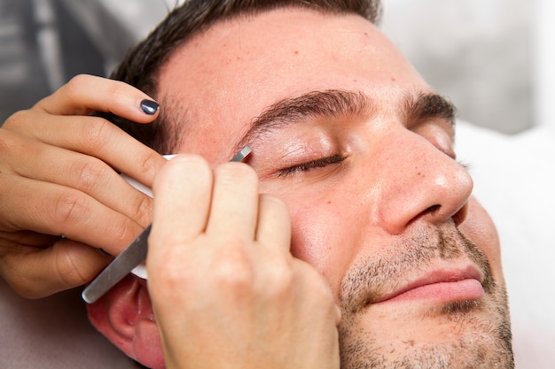 Beautician plucking a beautiful man eyebrows with tweezers in a beauty salon 