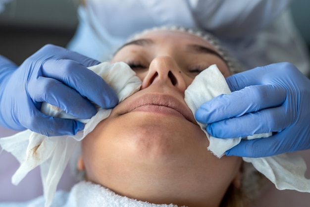 Beautician prepares a woman for the procedure and clean face skin with cotton pad