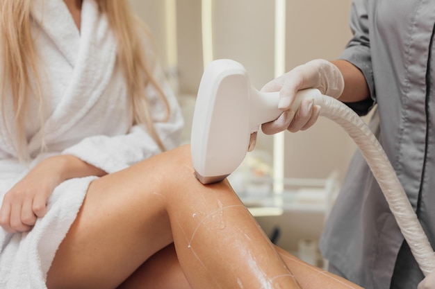 Beautician removes hair on beautiful female legs using a laser hair removal in beauty clinic