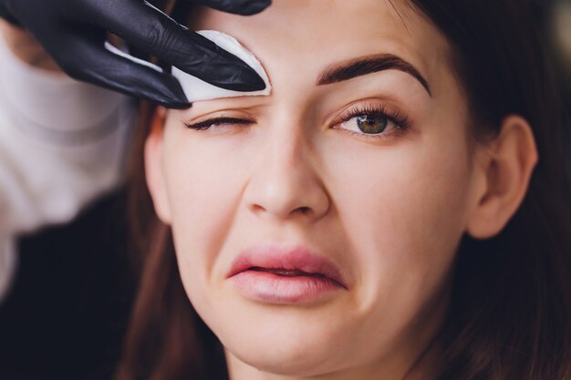 Beautician removing paint from client's eyebrow