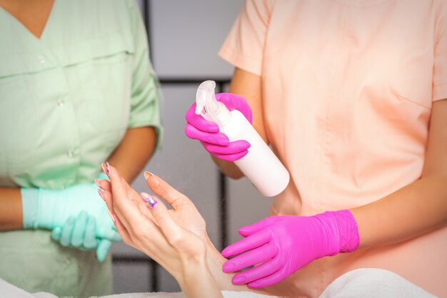 Beautician in rubber protective gloves disinfects hands of woman with antiseptic spray