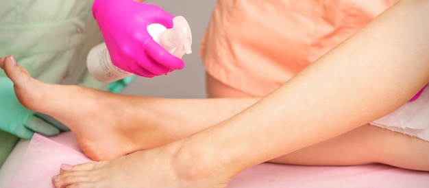 A beautician sprays a disinfectant on the feet of a young woman before the epilation procedure. Foot depilation.