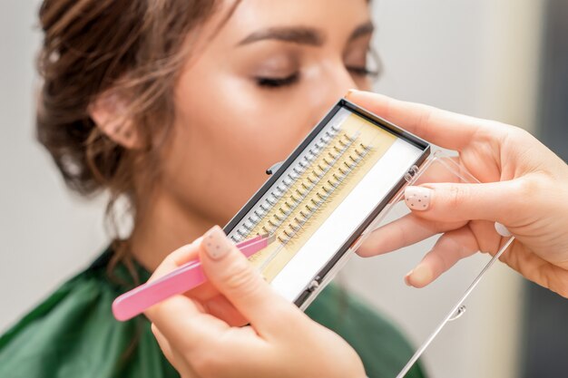 Beautician taking eyelashes by tweezers.