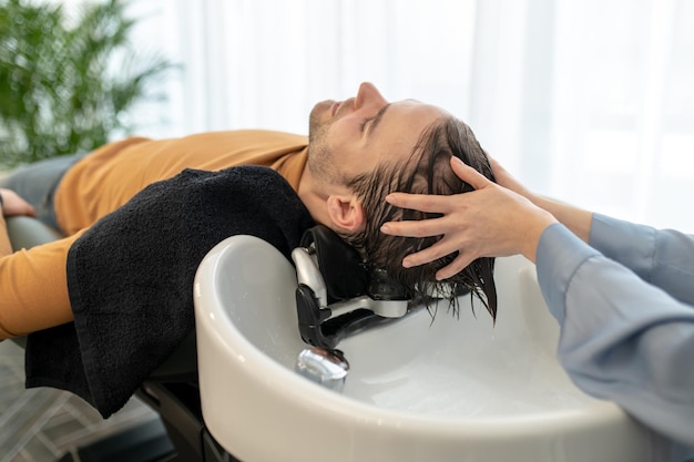 Косметолог моет волосы клиенту и массирует ему голову