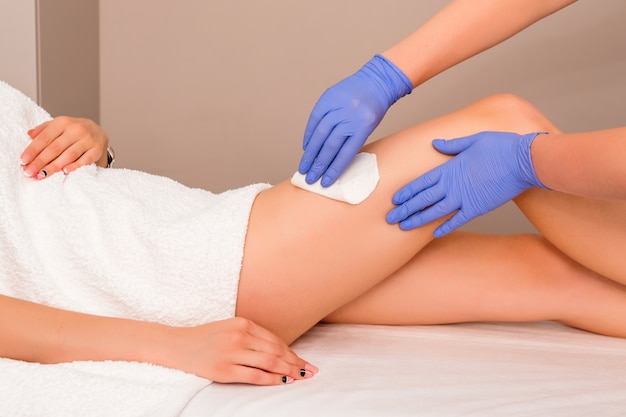 Beautician waxing female legs in spa center. Removing unnecessary hair on the legs.