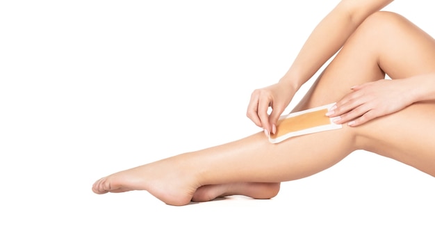 Photo beautician waxing female legs in spa center. well-groomed woman legs after depilation isolated on white background. waxing woman leg with wax strip at beauty spa. close-up waxing woman leg in spa.