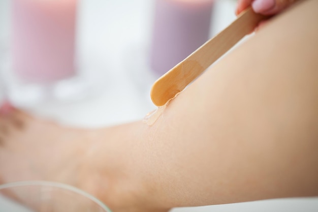 Beautician waxing female legs in spa center.
