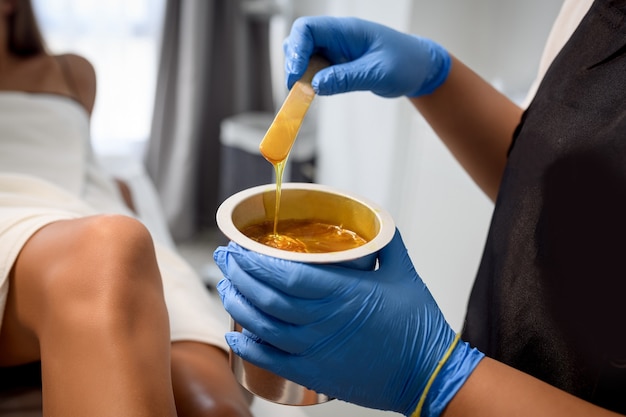 Beautician waxing female legs in spa center