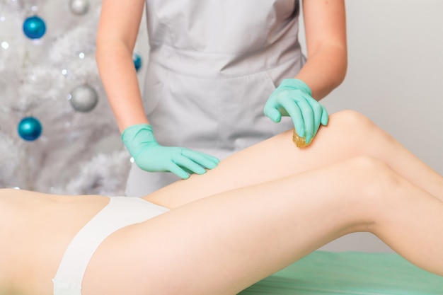 Beautician waxing legs of woman.