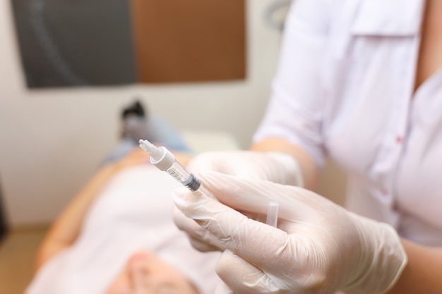 A beautician wearing sterile white gloves holds a hyaluronic acid injection filler