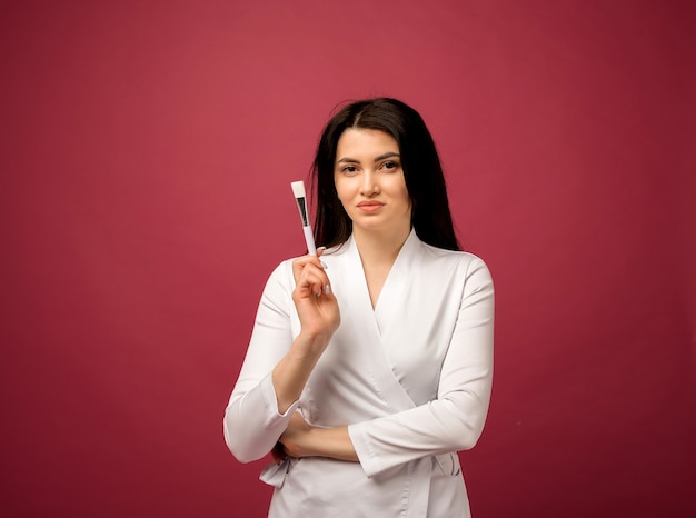 A beautician in a white medical suit holds a brush on burgundy