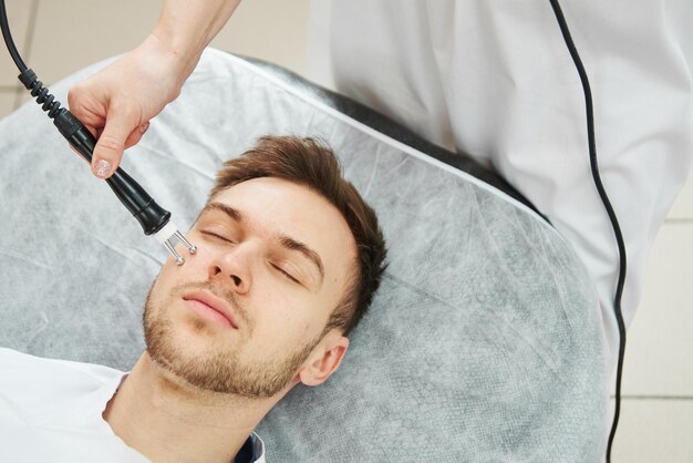 Photo beautician woman does the antiaging procedure of rf face skin lifting for a young man in a beauty parlor close up