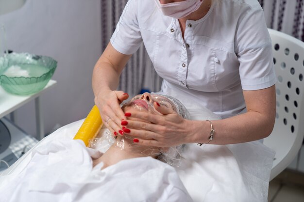 The beautician wraps the girl's face with a special film