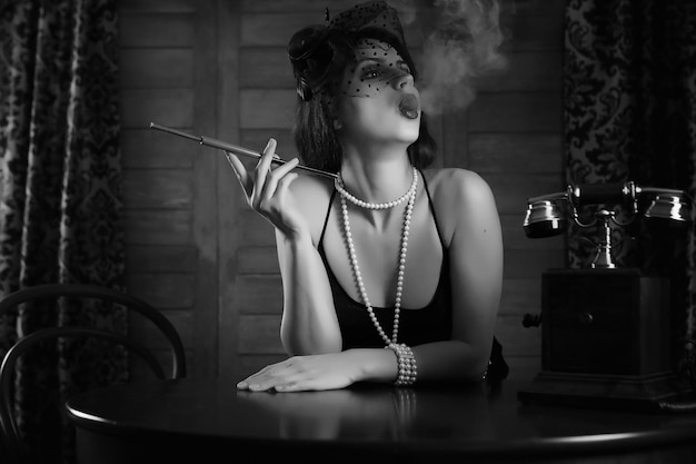 La bella ragazza degli anni '30 fuma una sigaretta al tavolo