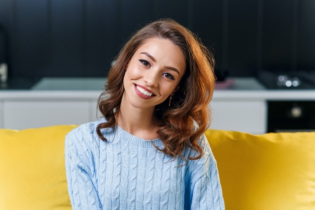 Beautiful 25-aged girl in soft blue sweater wearing glasses and looking at the camera with cute perfect smile on the background of stylish cuisine.