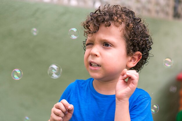 Beautiful 4-5 year old caucasian boy with curly hair in his backyard playing with soap bubbles