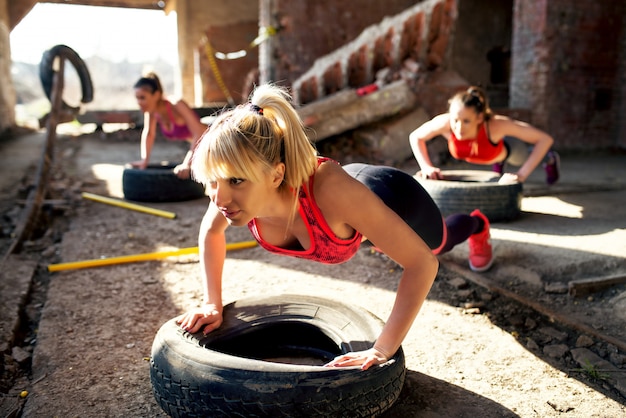 Beautiful active girls are doing push ups on tires in the old hangar.