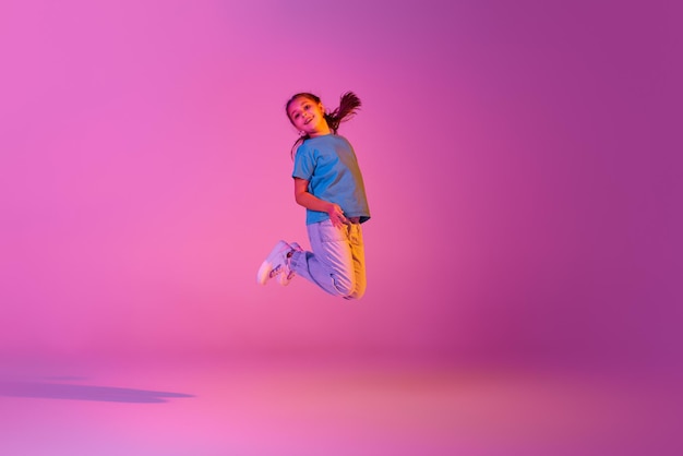 Красивая активная маленькая девочка прыгает, танцуя на розовом фоне в неоновом боевом танце