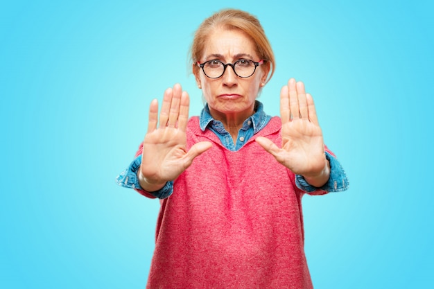 Foto bella donna bionda adulta segnalazione stop con il palmo della mano rivolto in avanti, con un serio e