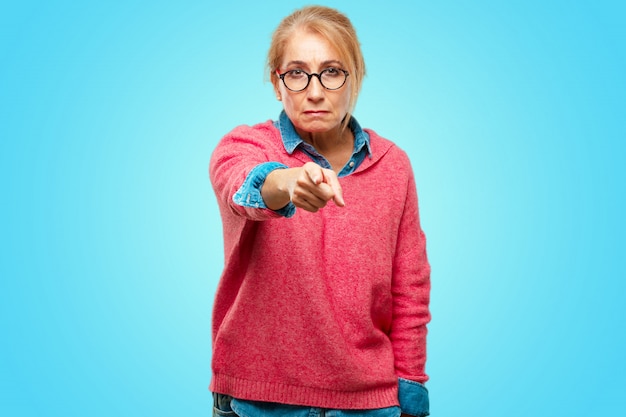 Foto bella donna bionda adulta che sorride felicemente e che indica in avanti con entrambe le mani, scegliendovi.