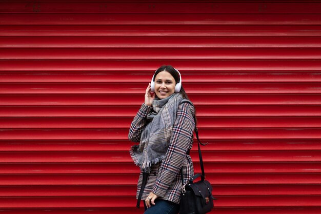 Beautiful adult caucasian woman in headphones with a smile on the background of a red embossed wall