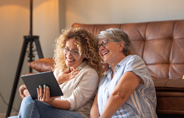 Bella figlia adulta con madre anziana seduta a casa a guardare i social media su tablet digitale