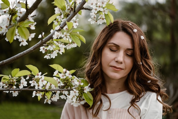 Bella donna adulta con gli occhi chiusi che si godono i fiori e l'odore dell'albero in fiore nel giardino primaverile closeup ritratto con trucco naturale