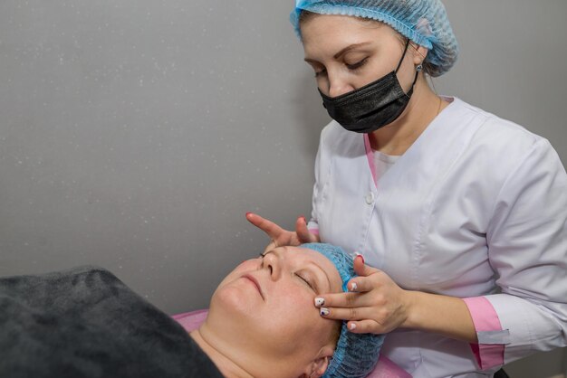 Beautiful adult woman enjoying facial massage at the spa. relaxing medical treatment and beauty concept. beautician in blue gloves makes facial massage to a client