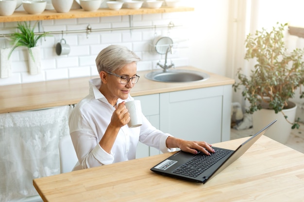 beautiful adult woman in glasses at the table with laptop at home with a mug