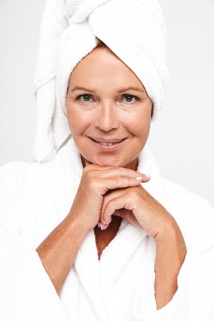 Photo beautiful adult woman wearing bathrobe and towel over her head smiling isolated over white wall
