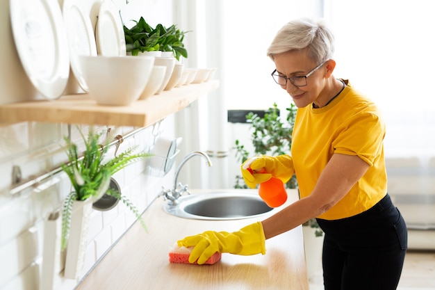 Bella donna adulta con gli occhiali in una maglietta gialla fa le pulizie di casa