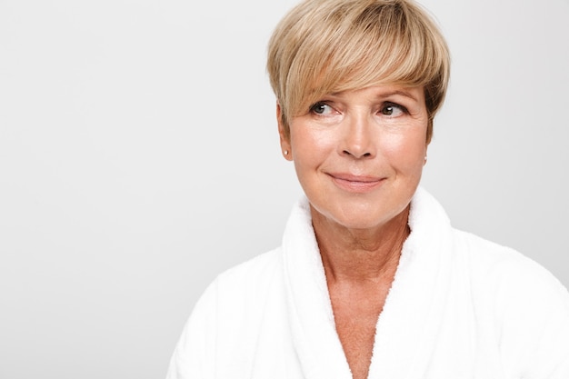  beautiful adult woman with short blond hair wearing white housecoat smiling isolated over white wall