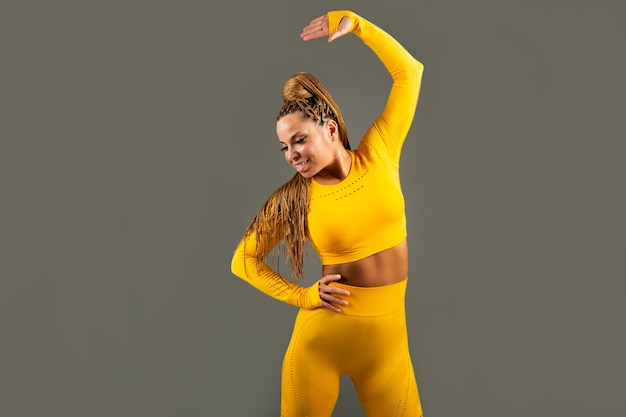 beautiful adult woman in a yellow tracksuit on a gray background is engaged in yoga