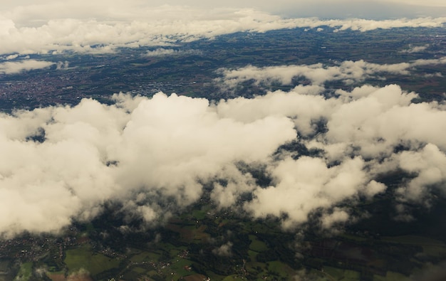 Красивый вид с воздуха на белые кучевые облака и землю с полями, деревьями и поселениями, вид крупным планом сверху из окна самолета