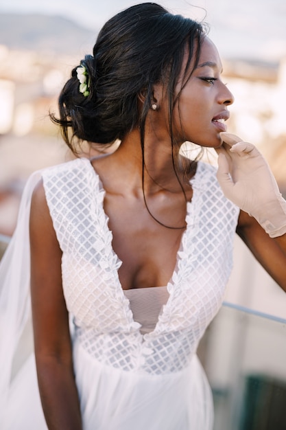 Beautiful African American bride in a white wedding dress, touches her face in vintage gloves