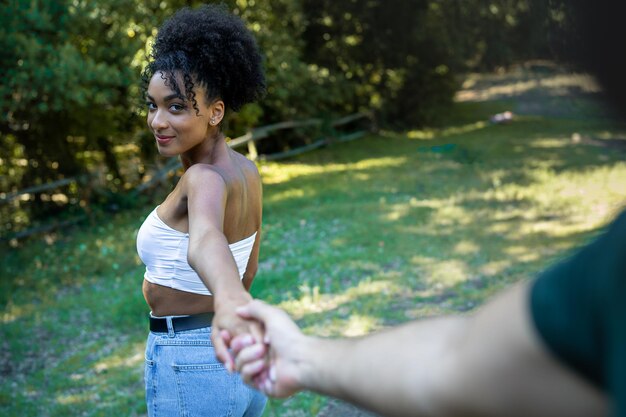 Photo beautiful african american girl holding caucasian mans hand and leading him outdoors in the countryside. multiracial love concept.