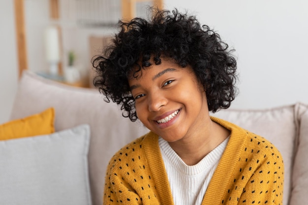 Beautiful african american girl with afro hairstyle smiling sitting on sofa at home indoor young afr