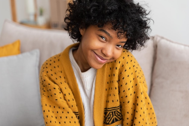 Beautiful african american girl with afro hairstyle smiling sitting on sofa at home indoor young afr