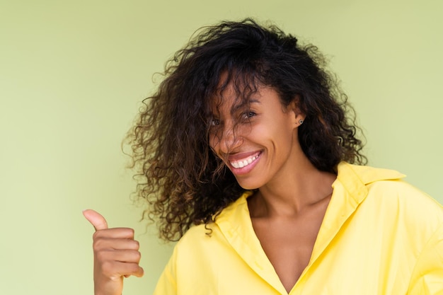 Beautiful african american woman in casual shirt on green background happy positive excited point finger to the left