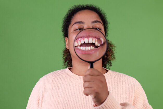 흰색 완벽한 치아를 보여주는 돋보기와 녹색 벽에 아름 다운 아프리카 계 미국인 여자