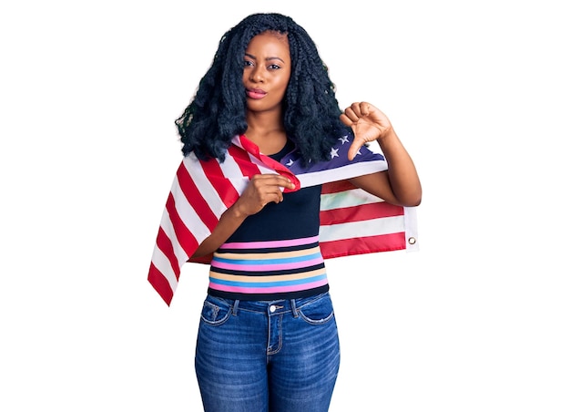 怒った顔でアメリカ合衆国の国旗を保持している美しいアフリカ系アメリカ人女性、親指を下にして嫌悪感を示す否定的なサイン、拒絶の概念
