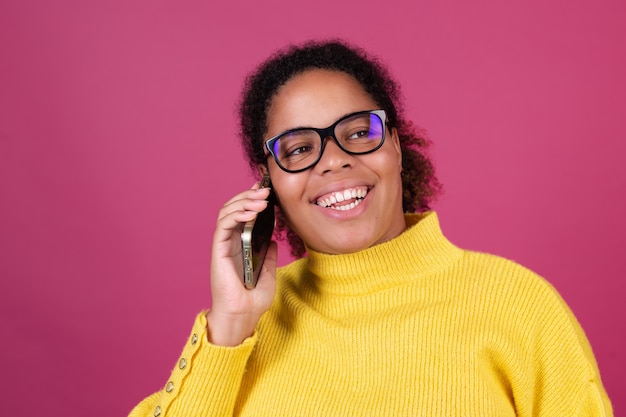 분홍색 벽에 있는 아름다운 아프리카계 미국인 여성이 휴대전화로 대화를 나누고 있습니다.
