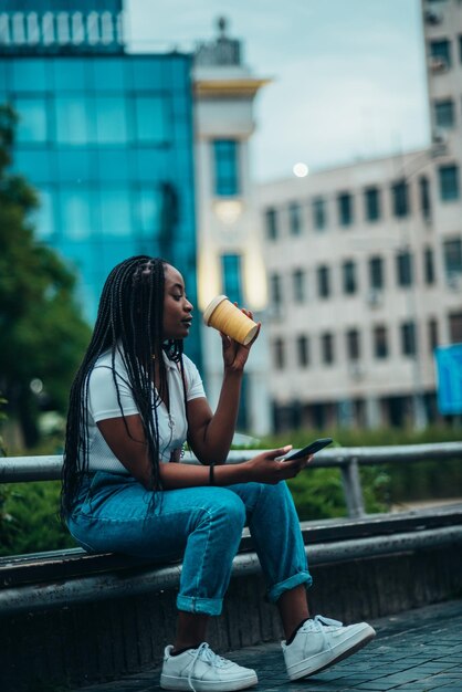 스마트폰을 사용하고 커피 테이크아웃을 마시는 아름다운 아프리카계 미국인 여성