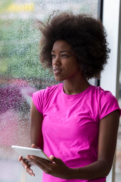 Bella donna afroamericana che utilizza il computer tablet da casa mentre la pioggia e il maltempo sono all'aperto