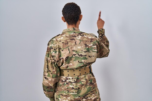 Beautiful african american woman wearing camouflage army uniform posing backwards pointing ahead with finger hand