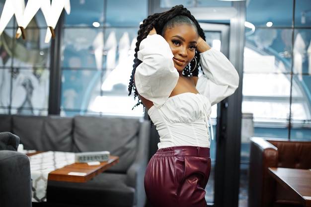 Beautiful african american woman in white blouse and red leather pants pose at restaurant