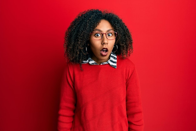 Beautiful african american woman with afro hair wearing sweater and glasses afraid and shocked with surprise and amazed expression fear and excited face